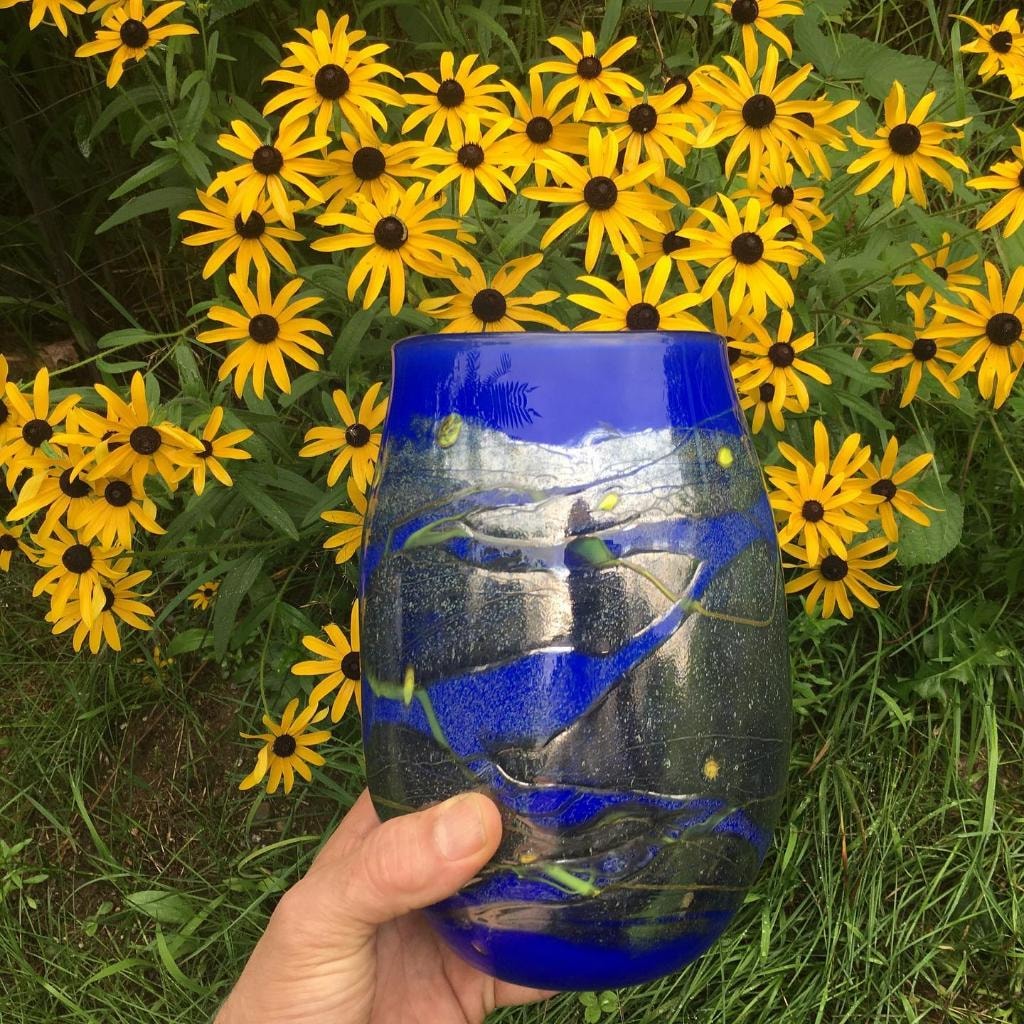 Blue strata vase held in front of yellow flowers